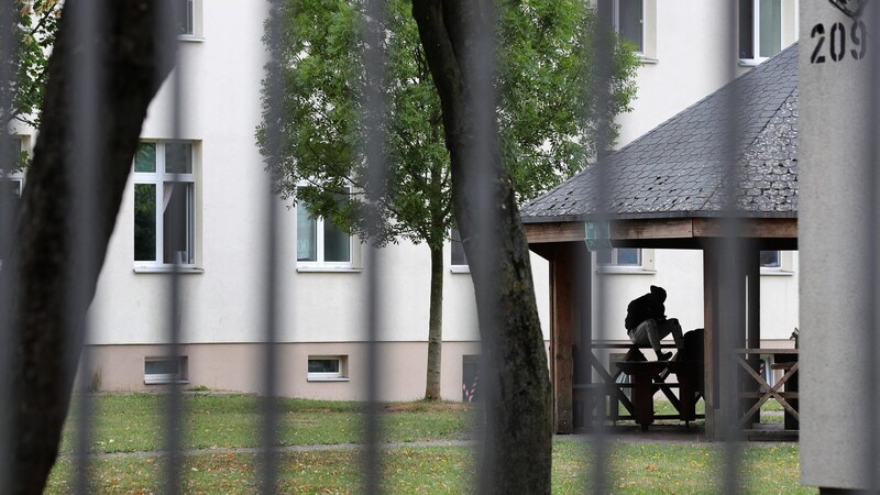 Ein Asylsuchender sitzt vor einem Wohnblock im Ankerzentrum Schweinfurt. Laut Innenminister Herrmann leben aktuell 66 000 Menschen in Ankerzentren und Sammelunterkünften in Bayern.
