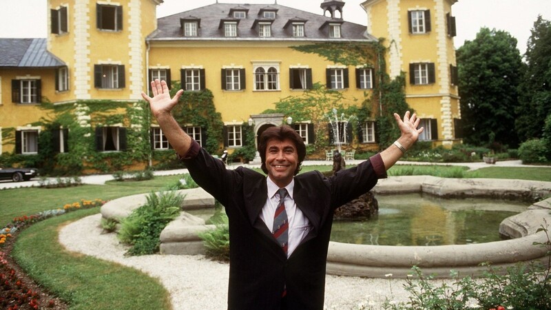 Schlagerstar Roy Black steht mit erhobenen Armen vor dem Schloss am Wörthersee bei Velden in Kärnten (Österreich), Schauplatz der RTL-Serie "Ein Schloss am Wörthersee", aufgenommen am 21.05.1990. Zu den Dreharbeiten soll Black immer mit dem Volvo gefahren sein, den Herbert Feldbauer zusammen mit seinem Bruder restauriert hat.